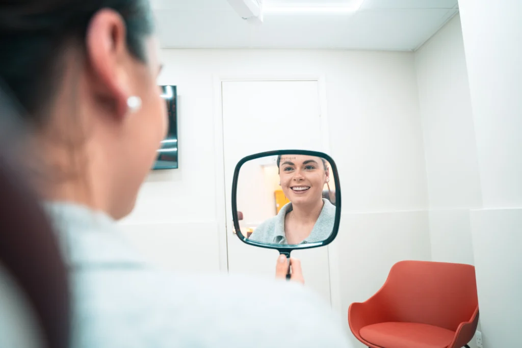 A patient smiling at her reflection in a hand mirror