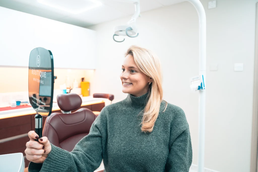 A Pearly Whites patient smiling at her whiter teeth in a hand mirror
