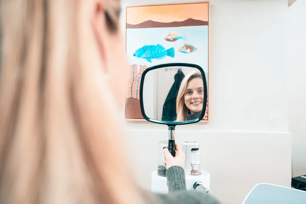 A patient smiling at her reflection in a hand mirror