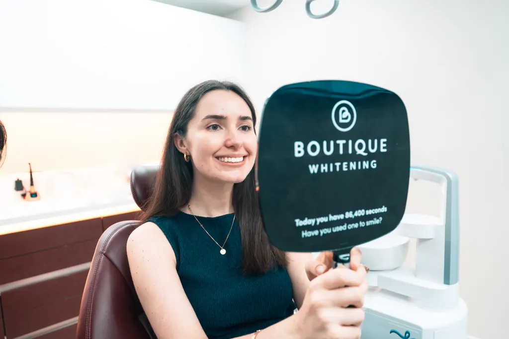 A Pearly Whites patient smiling at her new smile in a hand mirror