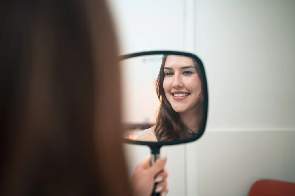 A patient smiling at her reflection in a hand mirror