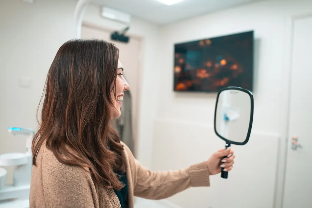 A patient smiling at her new teeth in a hand mirror