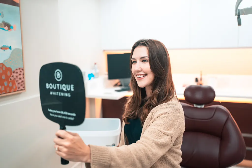 A patient smiling at her smile in a hand mirror