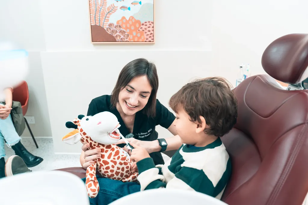 Dr Lia and Daisy the giraffe with a young patient in the dental chair